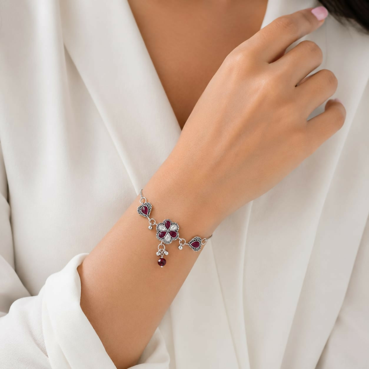 A woman's wrist wears an antique silver adjustable slider bracelet with a central flower, two hearts, and ruby-red pear