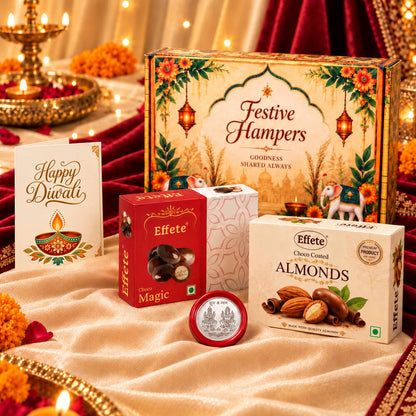 A decorative Diwali hamper box, two chocolate boxes, a greeting card, and a silver coin on a cream fabric.