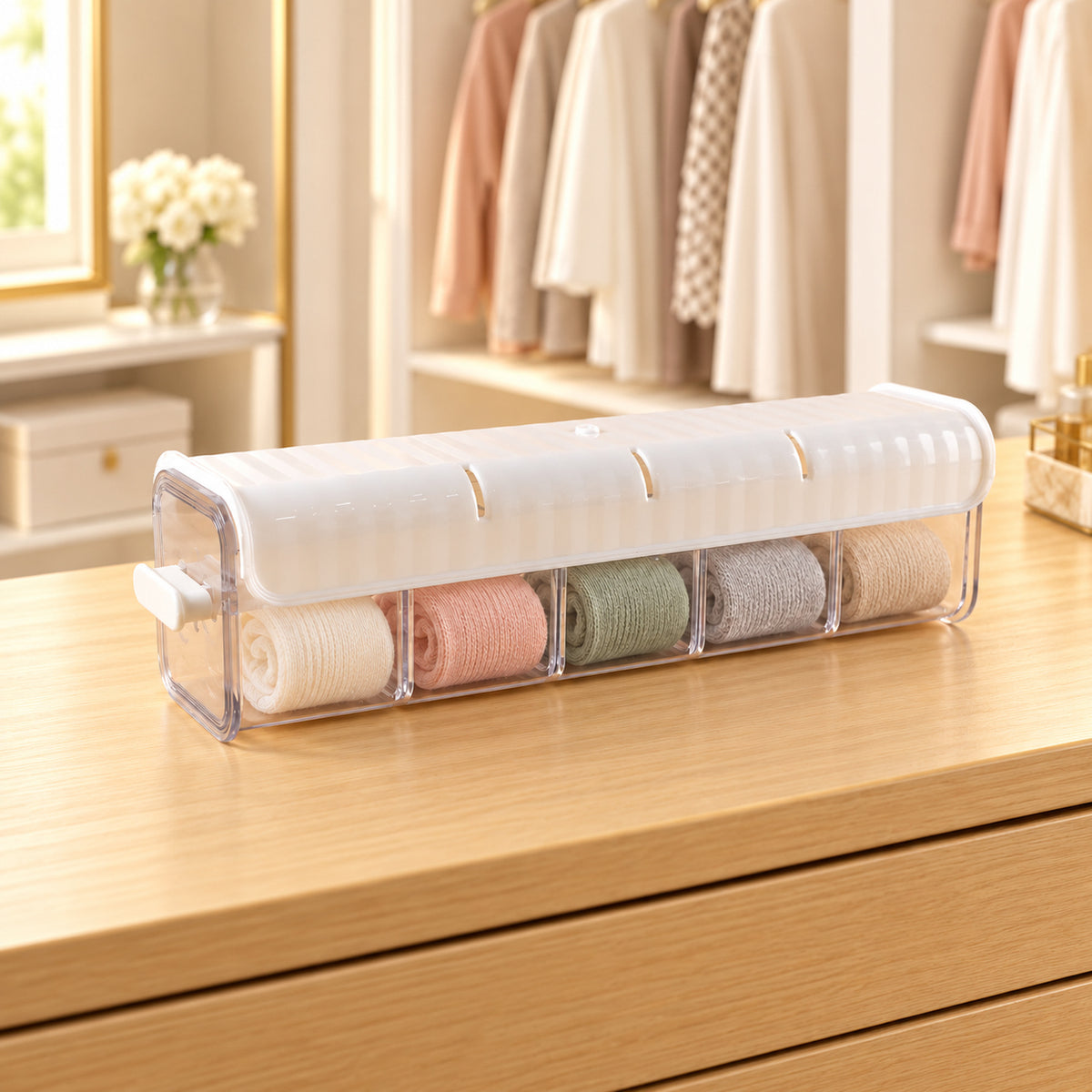 A white and clear plastic organizer with five compartments filled with rolled garments sits on a wooden dresser.