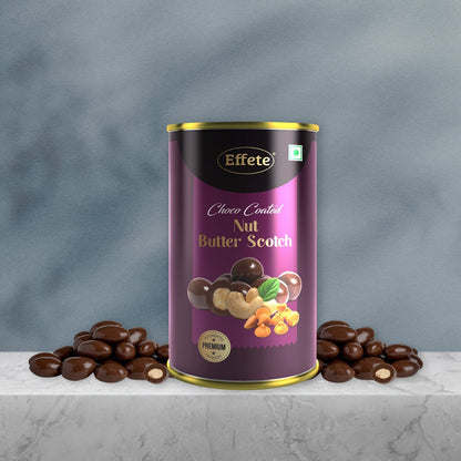 A purple and gold tin of chocolate-coated nuts sits on a marble surface, flanked by two piles of chocolate-covered nuts.