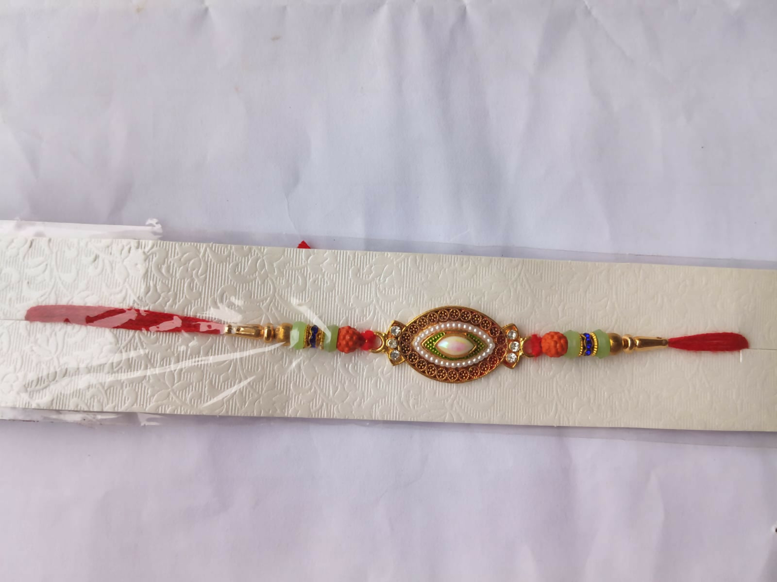 A decorative bracelet with a central oval stone and colorful beads is displayed on a textured white paper background.
