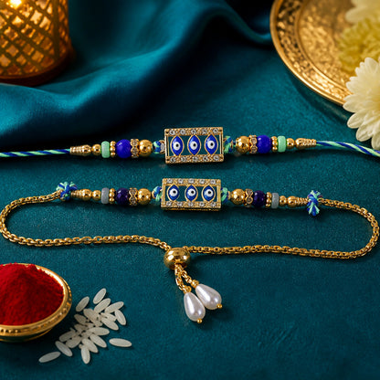 Two blue and gold evil eye rakhis, one a bracelet, on a dark teal fabric with rice and a golden bowl.