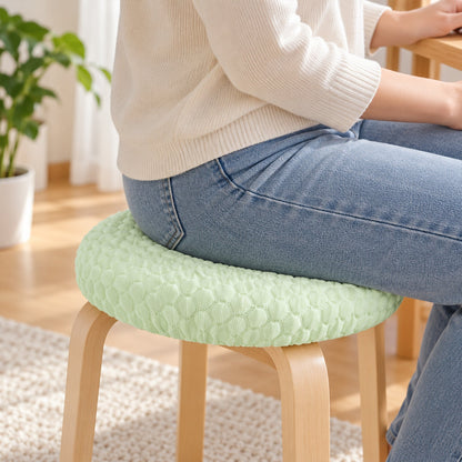 Person wearing blue jeans sitting on a light green textured round stool cushion cover on a wooden stool.