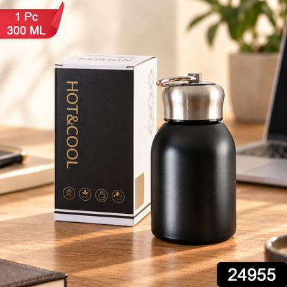 A black vacuum bottle with a silver cap and carry ring is shown next to its packaging on a wooden desk, with a red banner