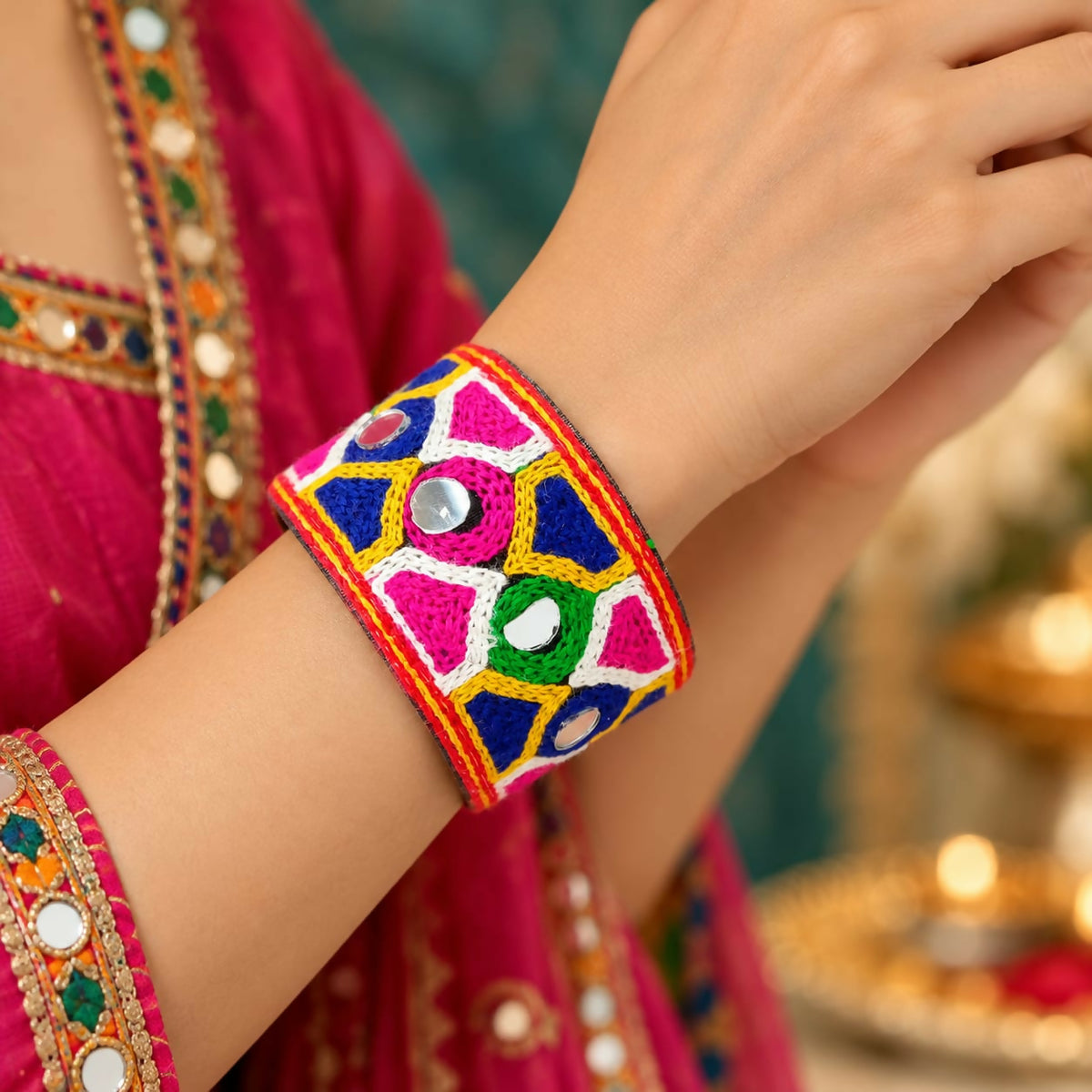 A woman's arm wears a wide, colorful embroidered cuff bracelet with small circular mirrors.