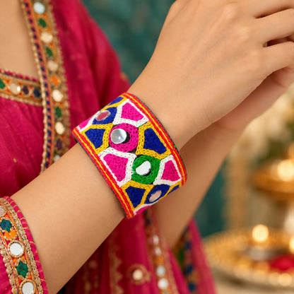 A woman's arm wears a wide, colorful embroidered cuff bracelet with small circular mirrors.