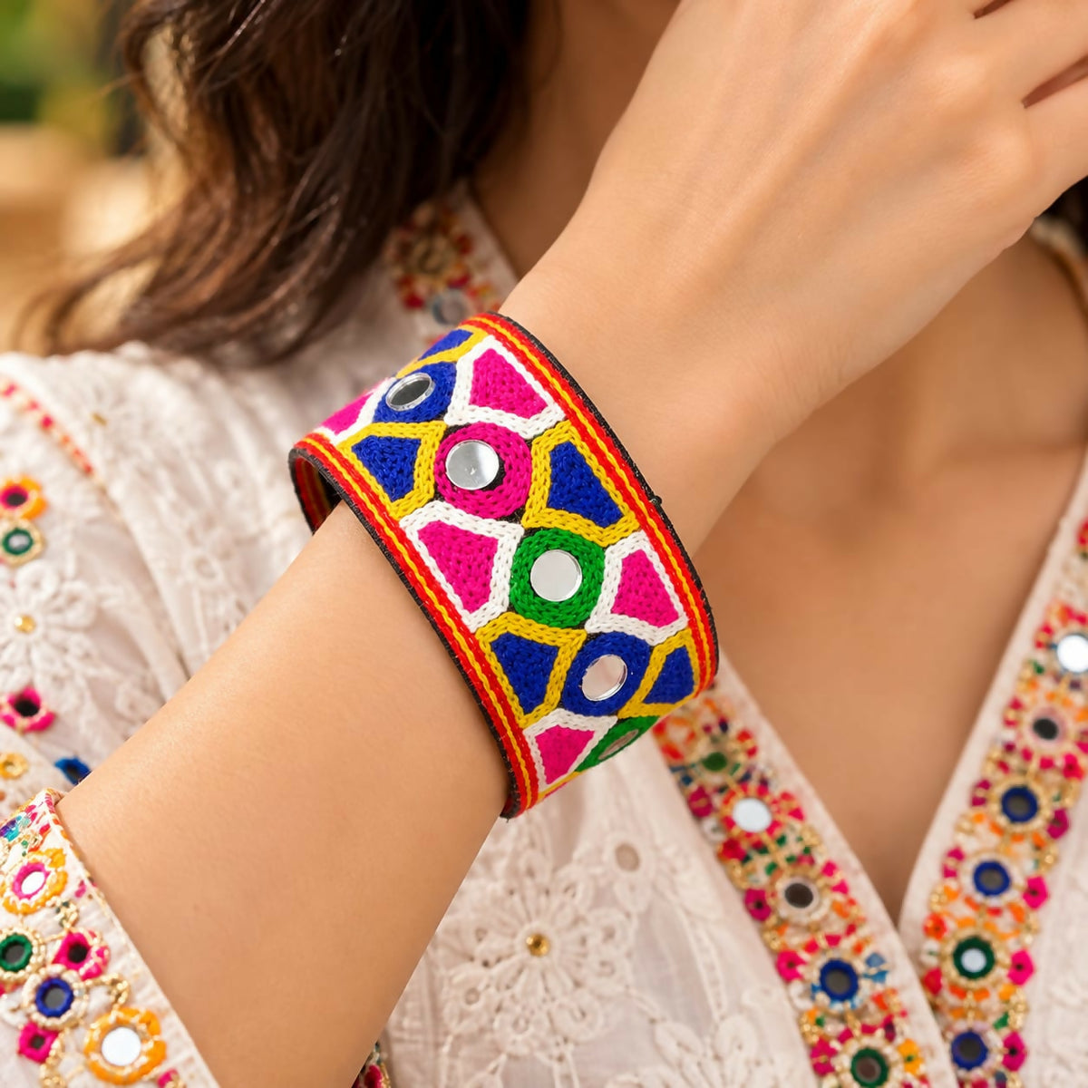 A woman's arm, adorned with a white and gold embroidered top, displays a bright mirror-embellished cuff.