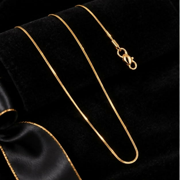 The long gold-tone snake chain necklace with its clasp is elegantly arranged on a dark fabric with a ribbon.