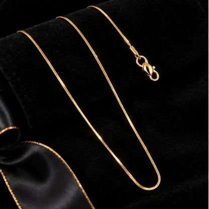 The long gold-tone snake chain necklace with its clasp is elegantly arranged on a dark fabric with a ribbon.