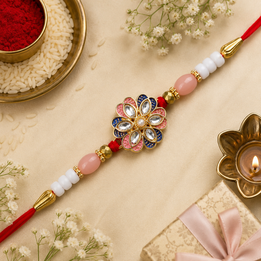 A red thread with pink and white beads, gold accents, and a central floral charm with pink, blue, and clear stones, rests on