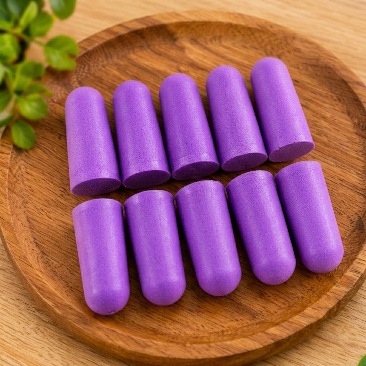 Ten individual purple foam earplugs are arranged in two rows on a round, light brown wooden plate.