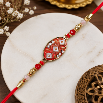 The red and gold Rakhi is displayed on a white marble coaster, surrounded by delicate white flowers and a carved wooden