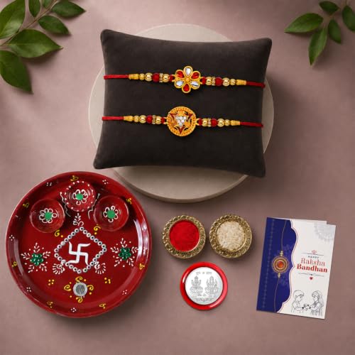A Rakhi gift set with two red and gold bracelets on a dark pillow, a red pooja thali, and small bowls of rice and kumkum.