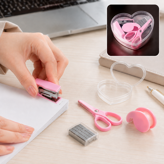 A person's hands operating a pink mini stapler on a stack of white paper, with other pink stationery items on a wooden desk.