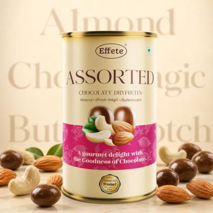 A tall beige tin of assorted chocolaty dry fruits is surrounded by loose cashews, almonds, and chocolate-covered dry fruits