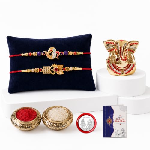 A gold Ganesh idol with red jewels stands on a white pedestal, with two red thread bracelets on a dark blue pillow, and