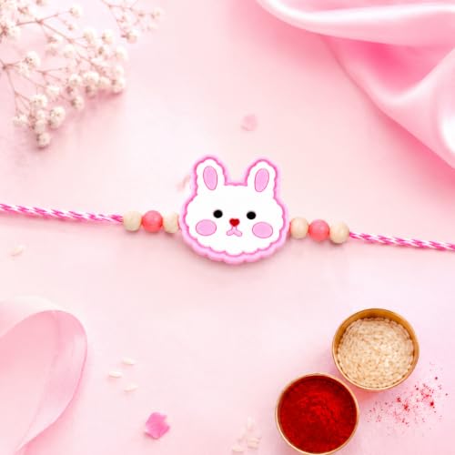 A pink and white bunny-shaped bracelet with pink and beige beads is centered on a pink background, with small bowls of rice