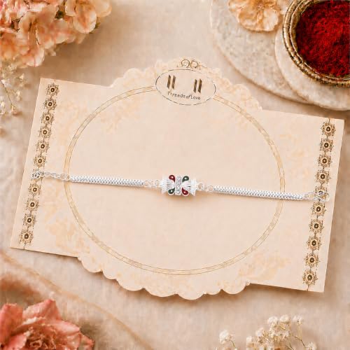 A silver bracelet with a red and green centerpiece is displayed on a decorative beige card with a patterned border.