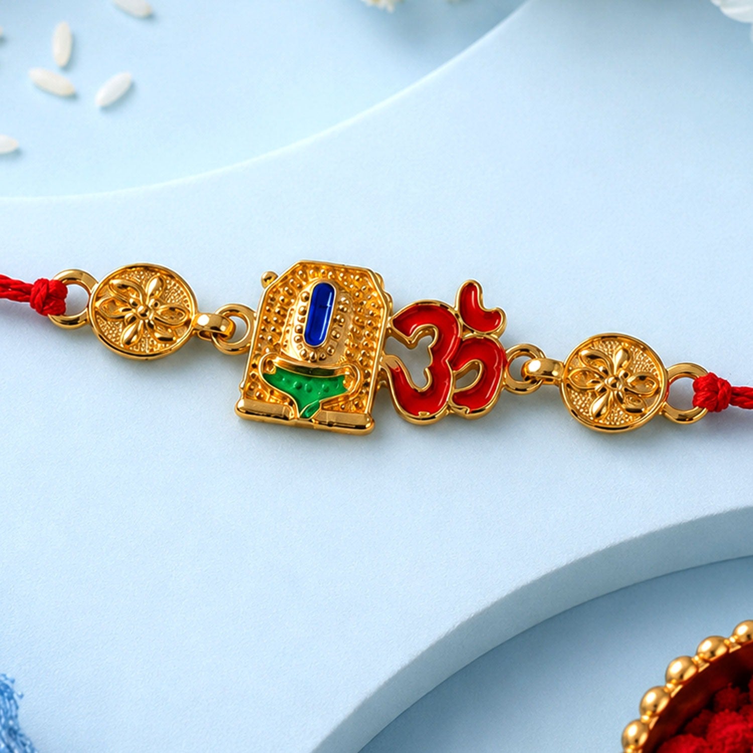 A gold-colored bracelet with a central blue and green enameled temple design and a red Om symbol, flanked by two floral