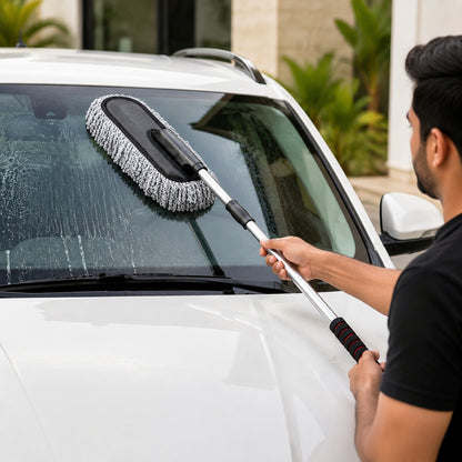 A person cleaning a white car's windshield with a gray and black microfiber duster with an extendable handle.