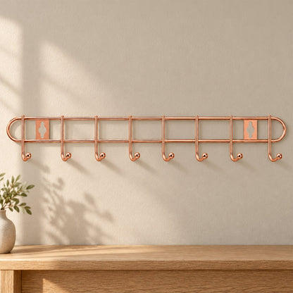 A rose gold metal wall hanger with eight hooks is mounted on a light beige wall above a wooden table.
