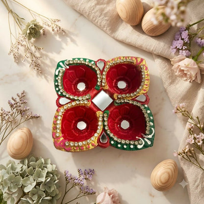 A colorful four-cup diya with mirror and stone embellishments is centered on a light surface with dried flowers and wooden