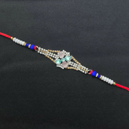 A red thread bracelet with a central diamond-studded floral design featuring pink and blue-green crystals, on a plain black