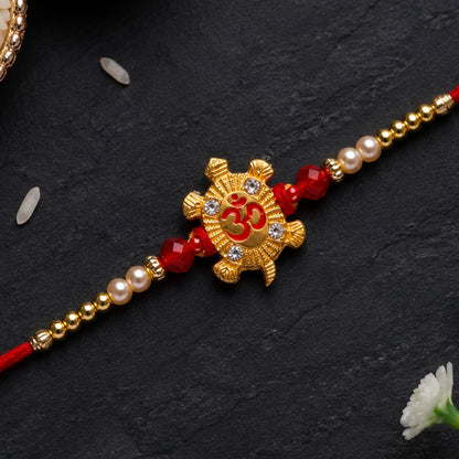 A red thread bracelet with a gold turtle charm, red beads, and white pearls on a dark background with scattered rice grains.