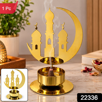 A golden metal incense holder with a crescent moon and mosque design, with a brown incense cone burning.