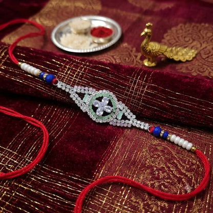 A red thread bracelet with a crystal-studded flower centerpiece and white and blue beads, resting on a rich red and gold