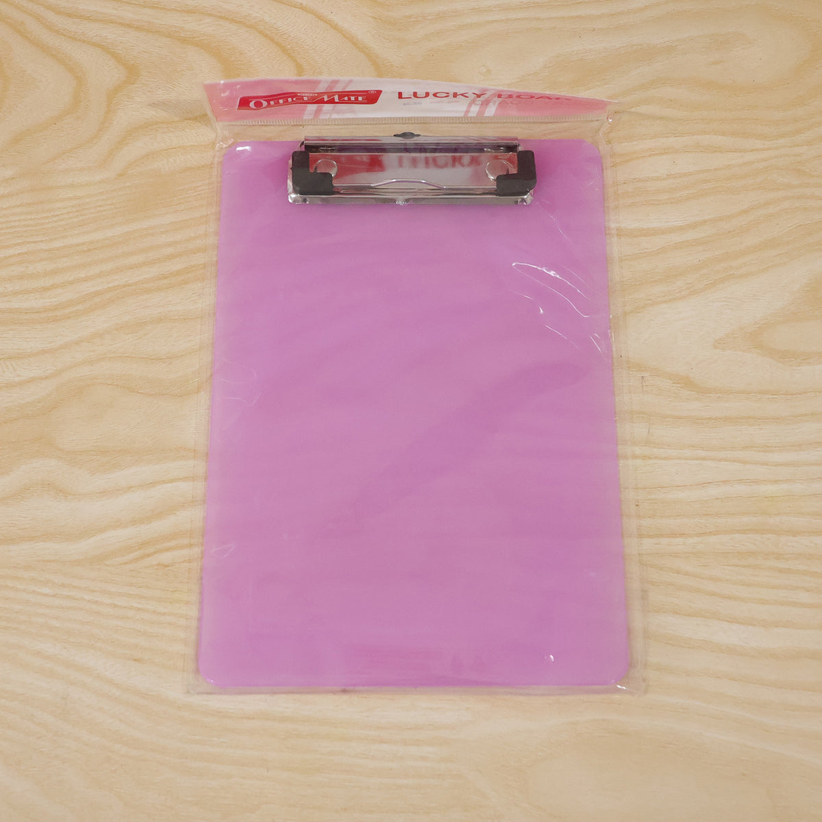 A new purple clipboard, still sealed in clear plastic packaging, rests on a light brown wooden surface.