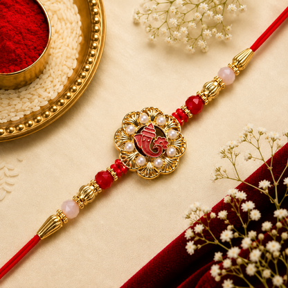 A red and gold Ganesha bracelet with red beads and golden detailing lies on a gold fabric, surrounded by white flowers and a