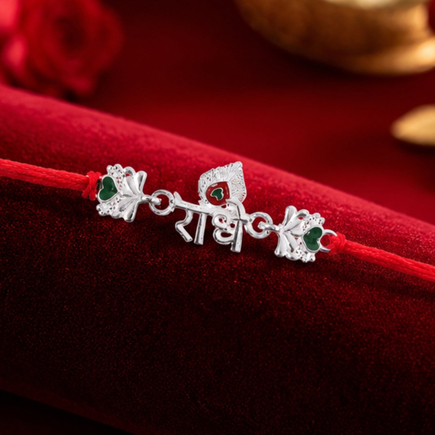 Silver Radhe Morpich Text Rakhi with Green Stones and Red Thread