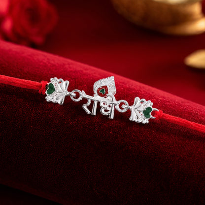 Silver Radhe Morpich Text Rakhi with Green Stones and Red Thread