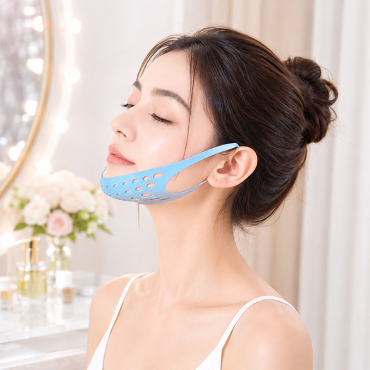 A woman with her eyes closed wears a blue silicone chin and ear strap with perforations, against a vanity background.