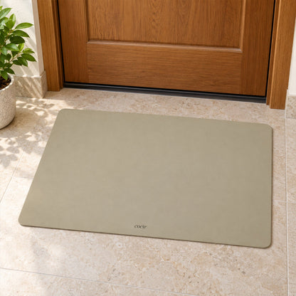 A light beige rectangular mat is positioned on tiled flooring in front of a closed wooden door.