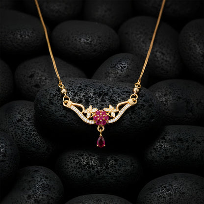 Gold finish floral necklace with red stone drop pendant worn on model's neck