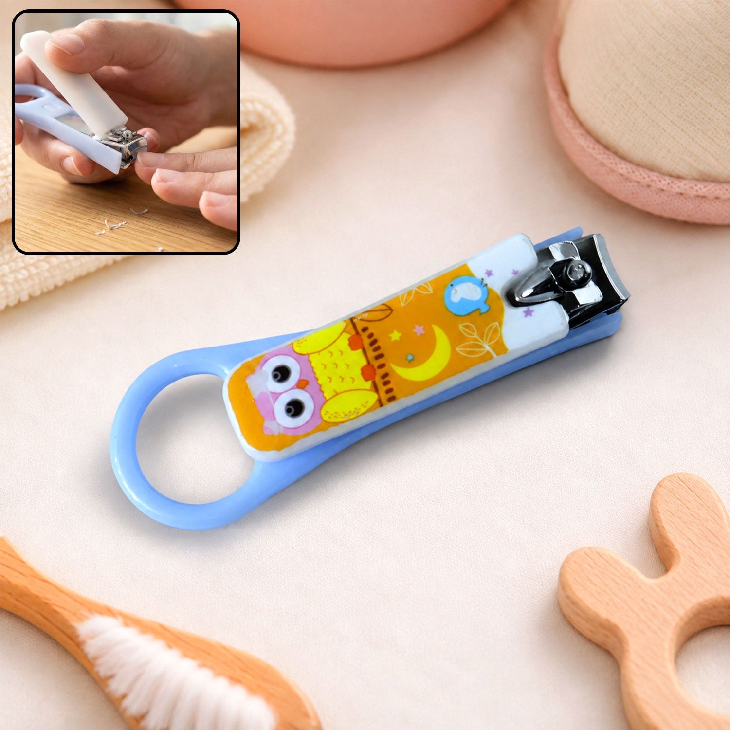 A light blue baby nail clipper with a yellow and white owl design, shown with an inset of it being used.