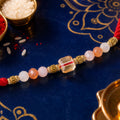 Red Thread Rakhi with Peach and Rose-Toned Crystal Bead Pendant
