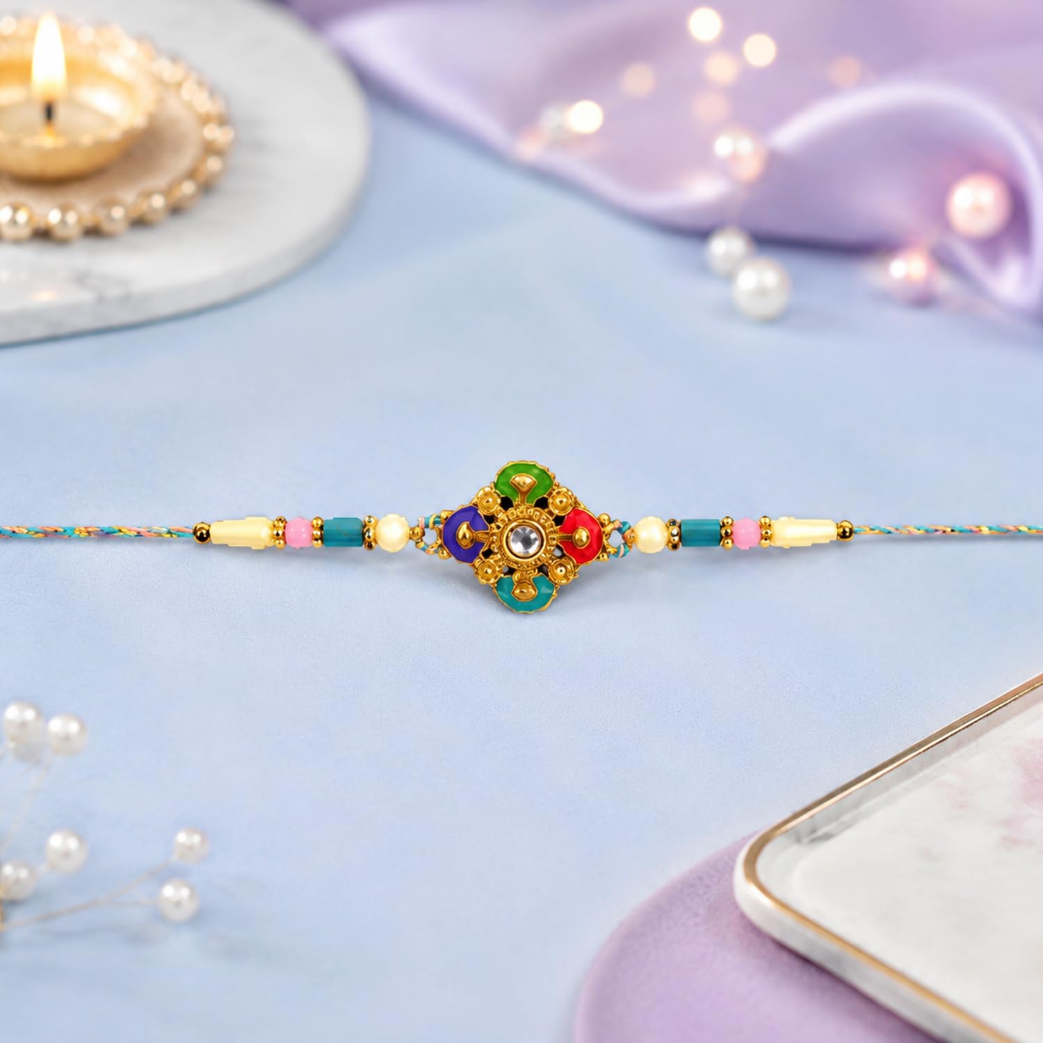 A single colorful Rakhi with a central floral design in green, blue, pink, and gold, adorned with a clear gem, is stretched