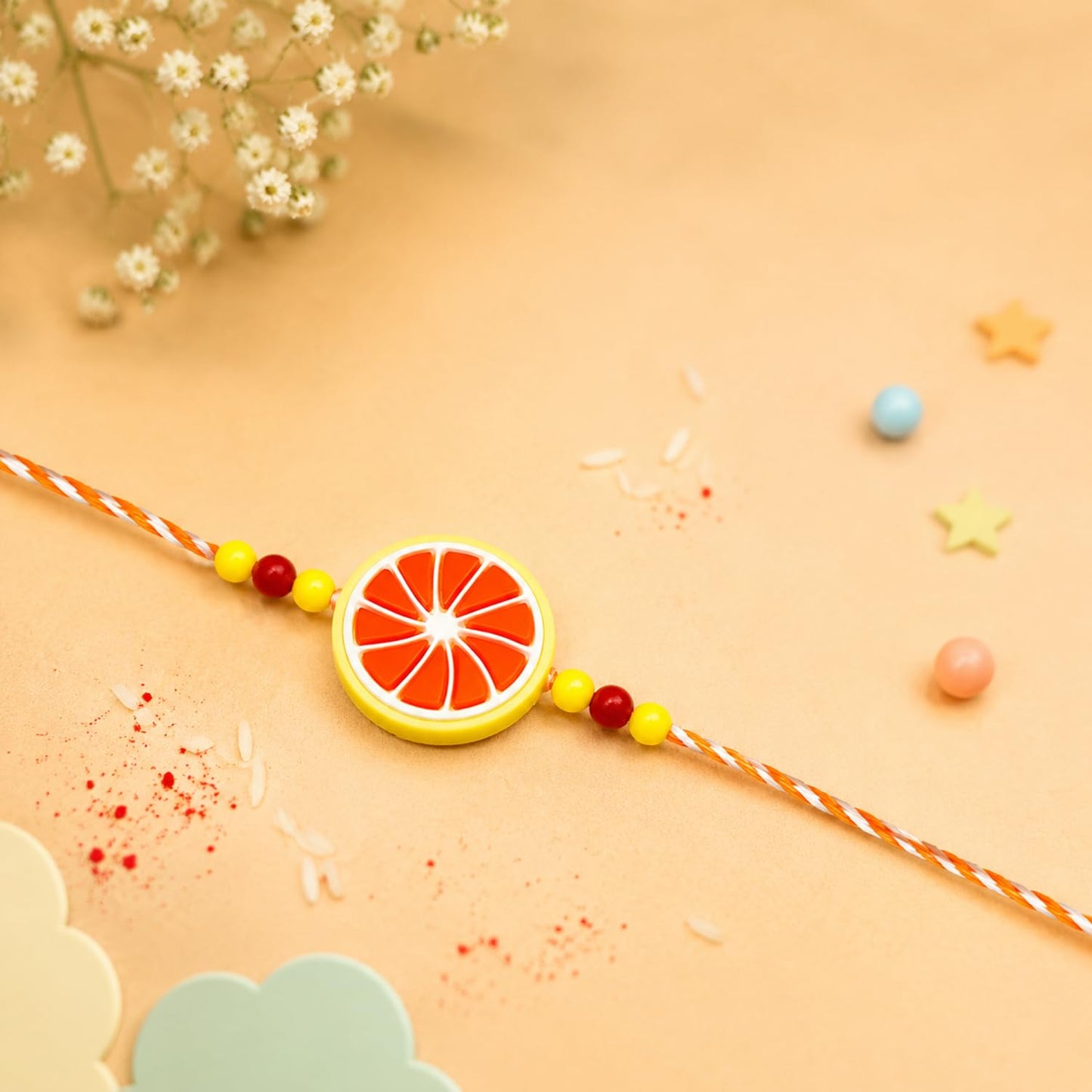 An orange and white citrus slice-shaped bracelet with red and yellow beads is centered on a light orange background with