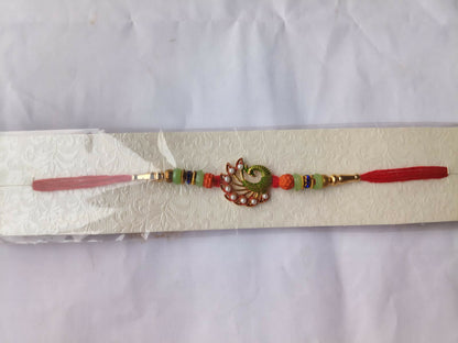 A red thread bracelet with a green peacock charm, orange and light green beads, and gold accents is packaged on a white card.