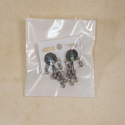 The oxidised silver long drop earrings with pink and turquoise stones and ghungroo bells are packaged in a clear plastic bag.