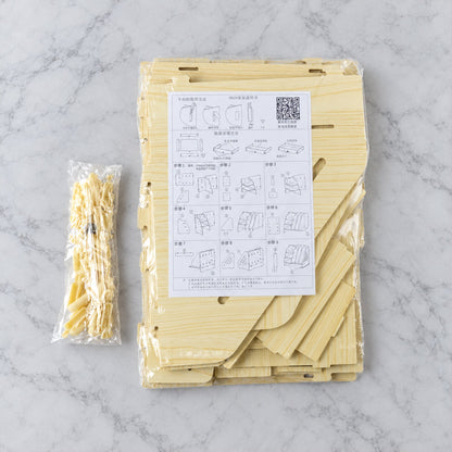 Disassembled wooden desk organizer pieces in clear plastic packaging with assembly instructions on a marble surface.