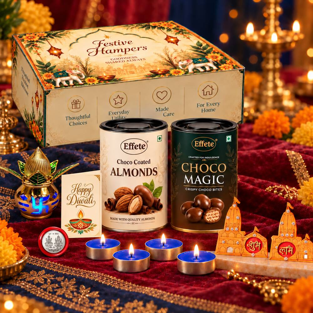 A Diwali gift set with a decorative box, two chocolate tins, a kalash, lit tealights, and a greeting card on a red cloth.