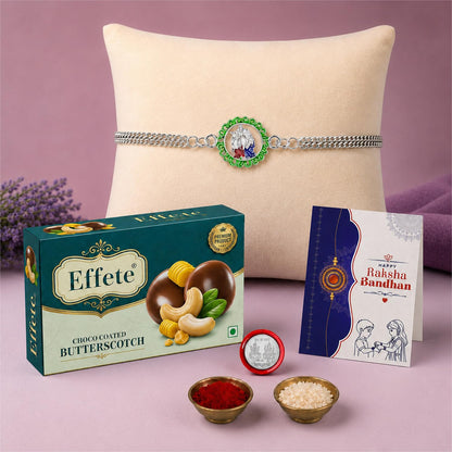 A Rakhi gift set with a silver bracelet on a pillow, a box of butterscotch, a card, and small bowls of rice and kumkum.