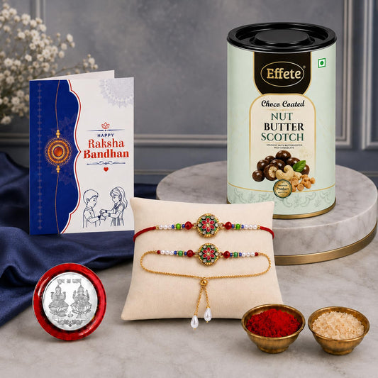 A Rakshabandhan gift set with a white card, a tin of butterscotch, two Rakhis on a pillow, a silver coin, and two small