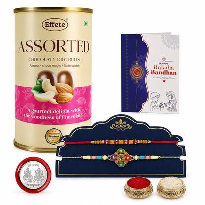 A tall beige tin of assorted chocolaty dry fruits stands next to a blue Rakhi card, two colorful Rakhis on a blue stand, a