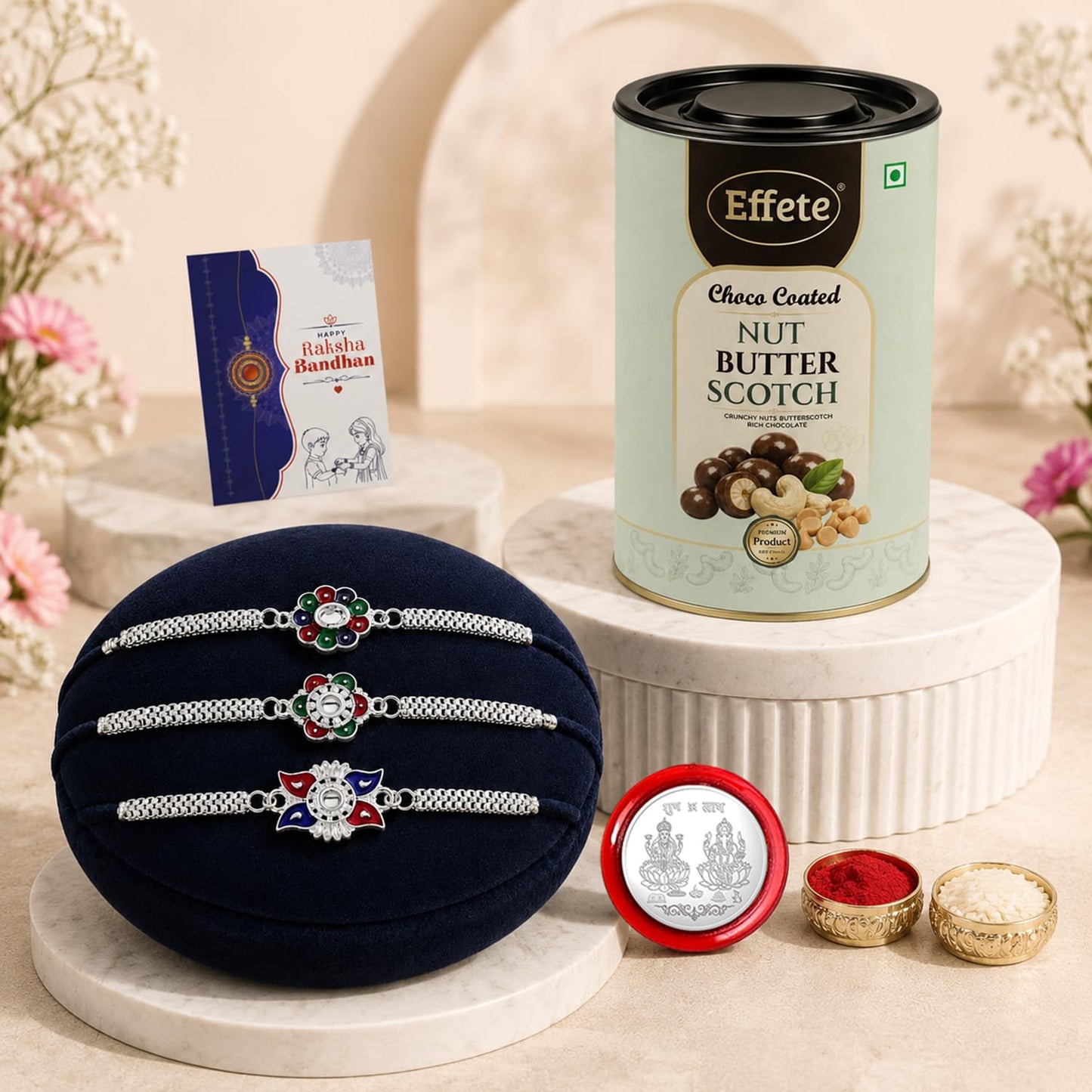 A navy velvet cushion displays three silver-toned bracelets with colorful, floral-shaped centers, alongside a chocolate tin,