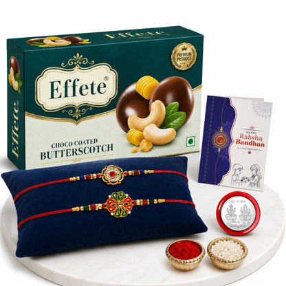 A white marble tray holds a teal box of Effete chocolates, two floral Rakhis on a blue cushion, a Raksha Bandhan card, and